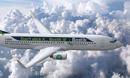 Large aeroplane in flight with Bostik banner